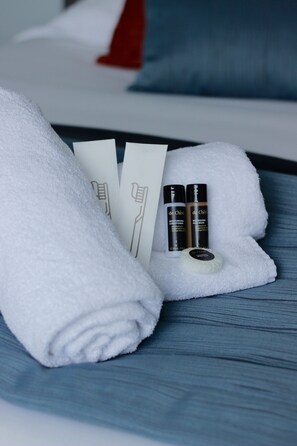 A neatly folded white towel on a bed with a blue headboard, accompanied by two toiletry bottles and a white bar of soap.