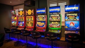 Una hilera de máquinas tragamonedas con pantallas iluminadas, cada una mostrando diferentes títulos de juegos y montos de premios.