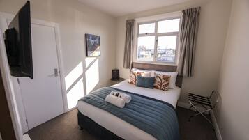 A hotel room with a bed, a flat-screen TV mounted on the wall, a window with curtains, and a painting on the wall.