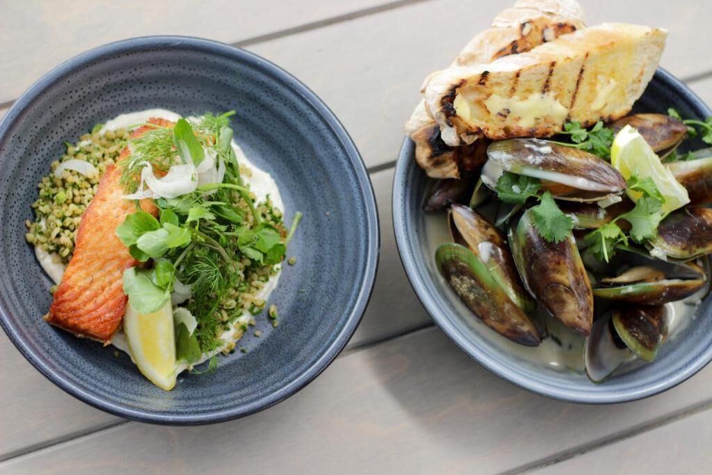 Zwei Schüsseln mit Essen, eine mit gegrilltem Fisch und Salat, die andere mit Muscheln und Salat.