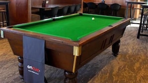 Una mesa de billar en una sala con zona de bar, asientos y una televisión en la pared.