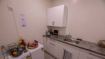 A small kitchenette with a coffee maker, toaster, and a sink. There are jars, a basket, and a cake on the counter.
