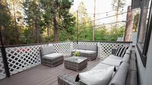 An outdoor deck with wicker furniture, a glass coffee table, and a white lattice fence. - Harte Of The Pines Pet Friendly Walk to Downtown (Twain Harte)