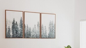 A brown leather sofa with three cushions, a large green plant, and three framed pictures of snowy forests on the wall. - Harte Of The Pines Pet Friendly Walk to Downtown (Twain Harte)