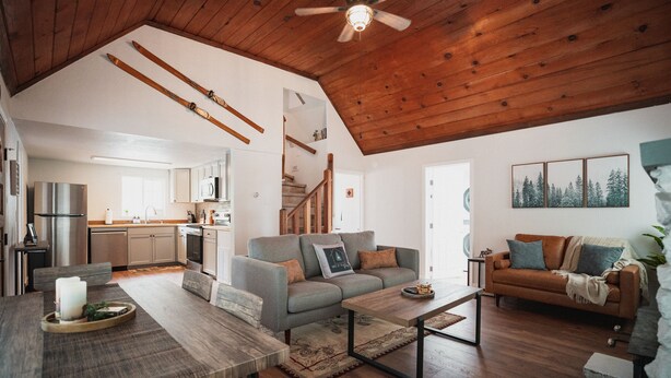 A spacious living area with a high ceiling, wooden beams, a sofa, a coffee table, and a dining table with a tray. - Harte Of The Pines Pet Friendly Walk to Downtown (Twain Harte)