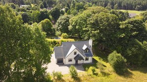 Een huis omgeven door dicht bos, met een verzorgd gazon en een cirkelvormige oprit.