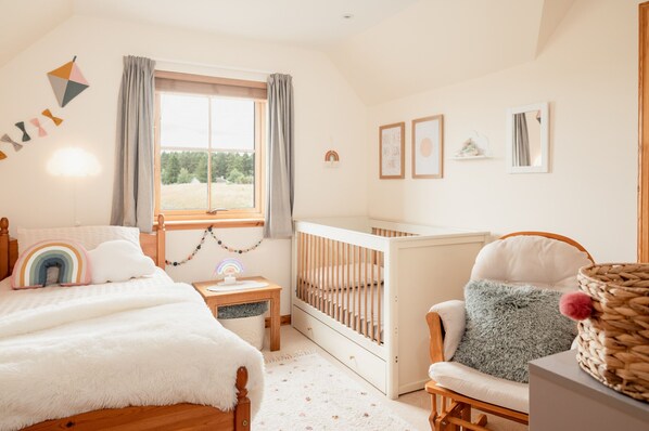 A cozy baby room with a crib, a rocking chair, a small table, and a window with curtains.