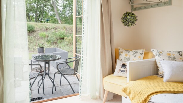 Een kamer met een bed, een raam met gordijnen, een hangplant en uitzicht op het omliggende landschap.
