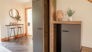 Een kamer met een houten kast, een ronde spiegel, een tafeltje met krukken en een plant in pot.