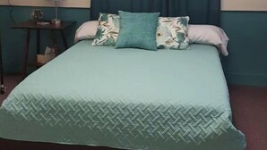 A bed with a patterned bedspread, a bedside table with a lamp, and a wall socket. - In the Heart of Historic Paoli (Paoli)
