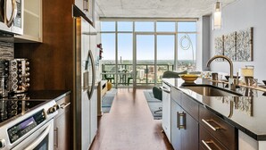 Een moderne keuken met roestvrijstalen apparatuur, een groot raam met uitzicht op een stadsgezicht, en een eethoek met een panoramablick.