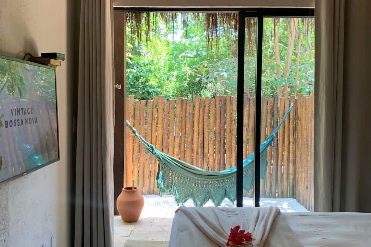Een kamer met een bed, een hangmat en uitzicht op een houten schutting en groen.