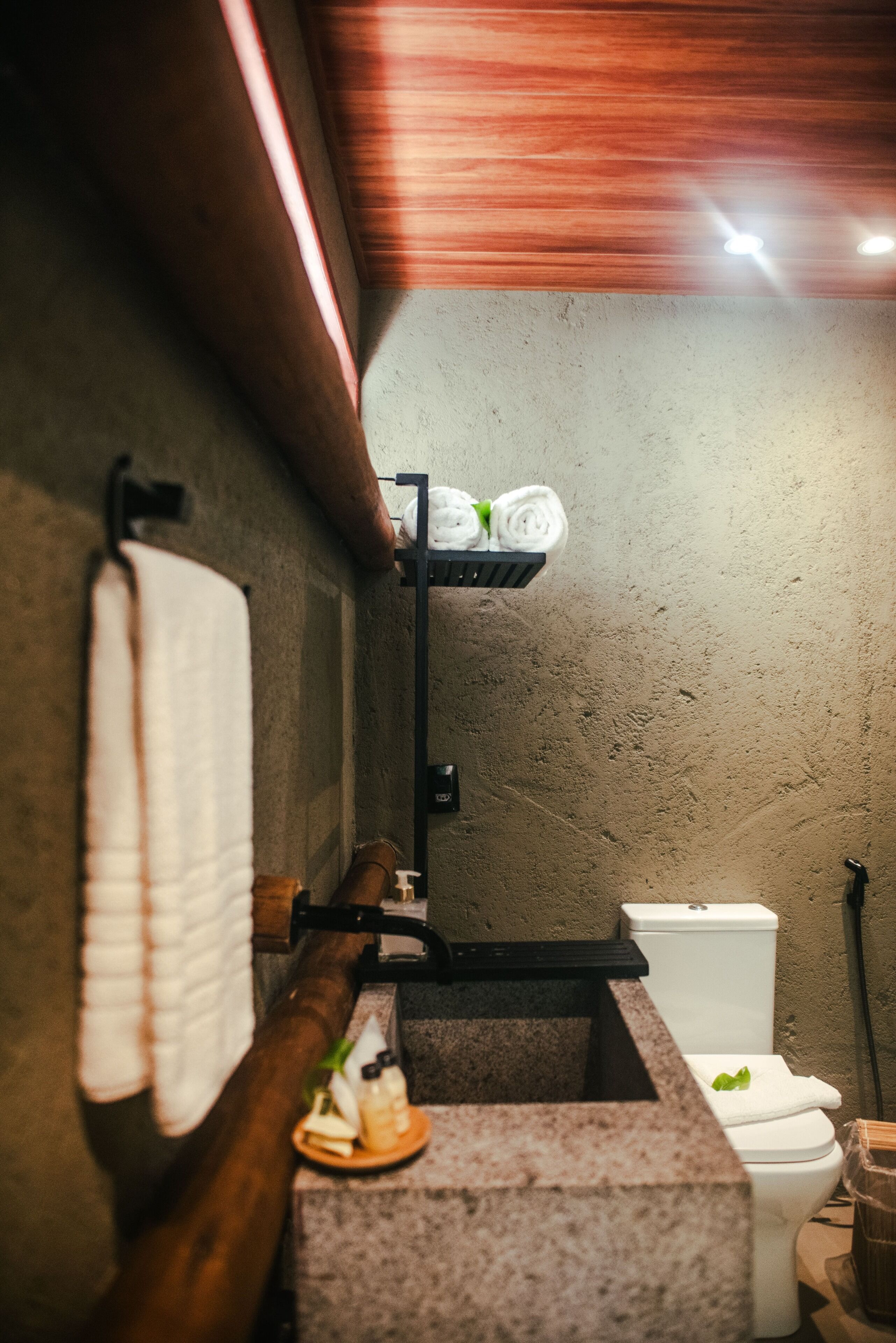Ein Badezimmer mit Marmorwaschbecken, einem Handtuchhalter mit gerolltem Handtuch, einer Toilette und einem Regal mit Handtüchern.