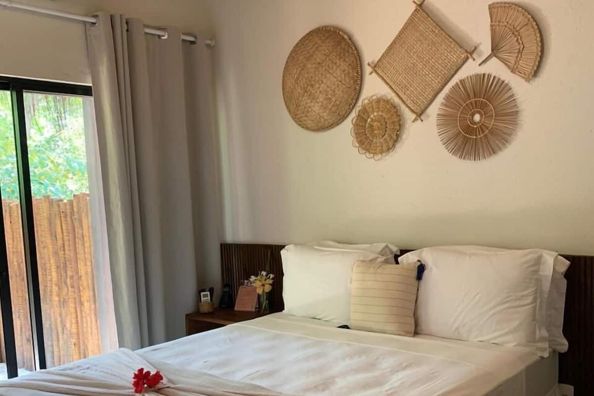 Een slaapkamer met een bed, nachtkastje, een luchtverkoeler aan de muur en een raam met gordijnen.