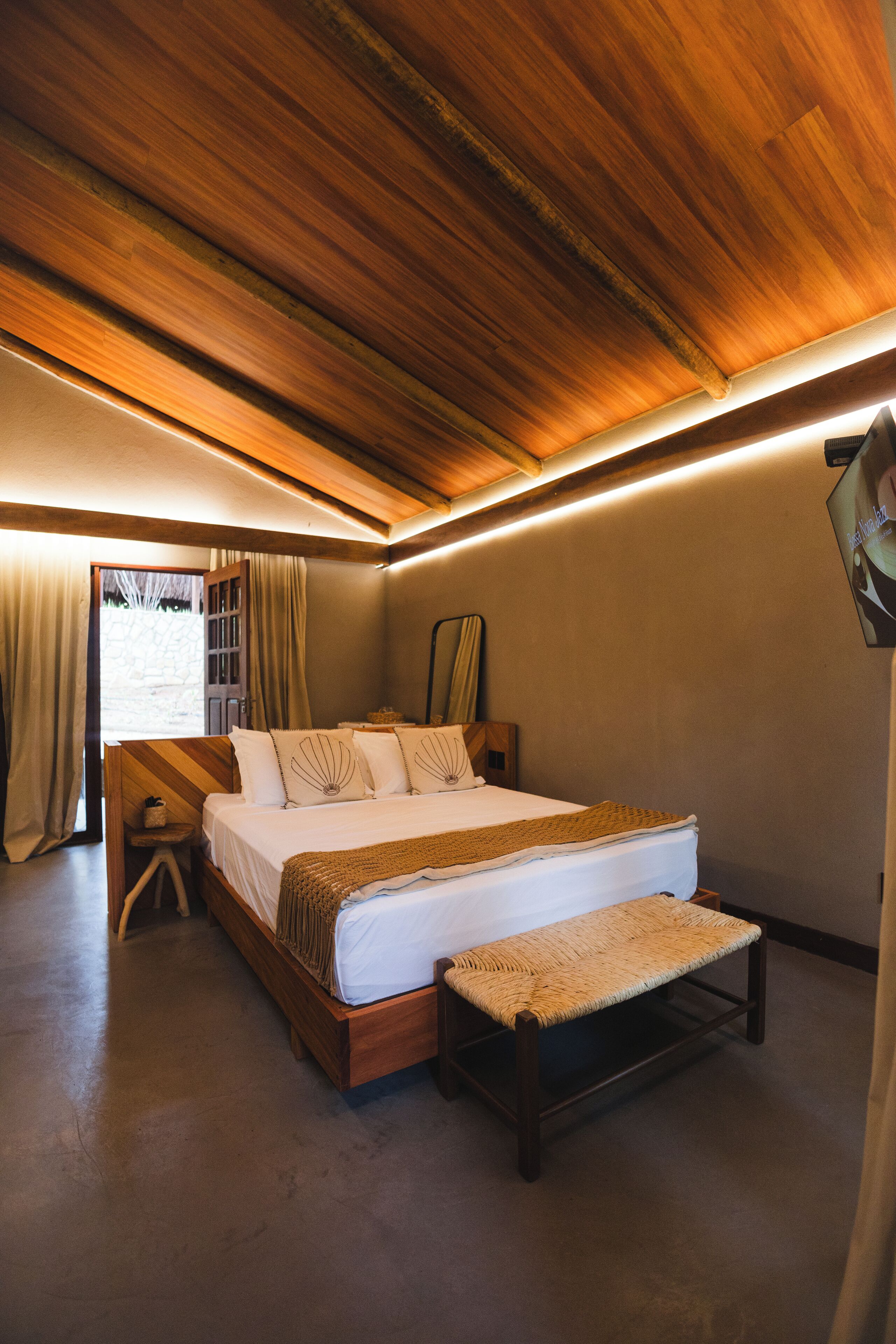 Un dormitorio con techo de madera, una cama con banqueta y vistas al exterior a través de una ventana.
