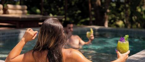 A person relaxing by a pool with another person in the background holding a drink.