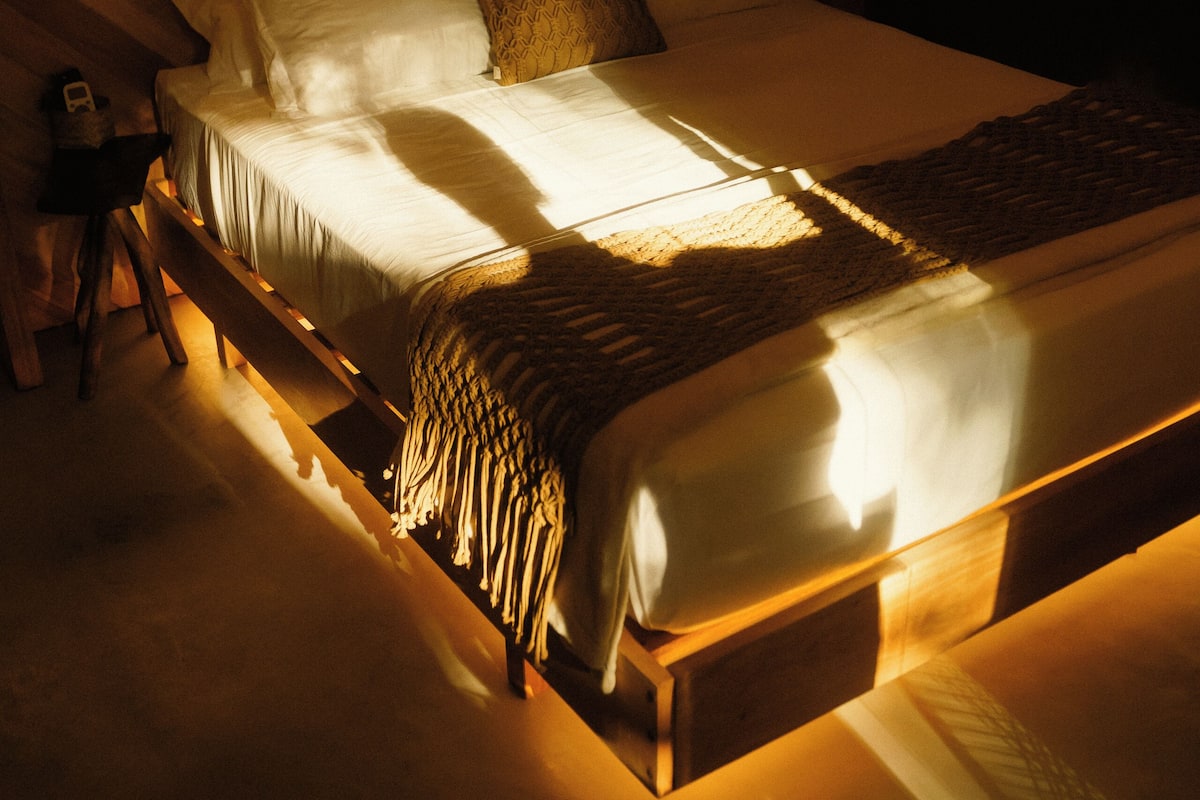 Een opgemaakt bed met hoofdbord, nachtkastje en lamp.
