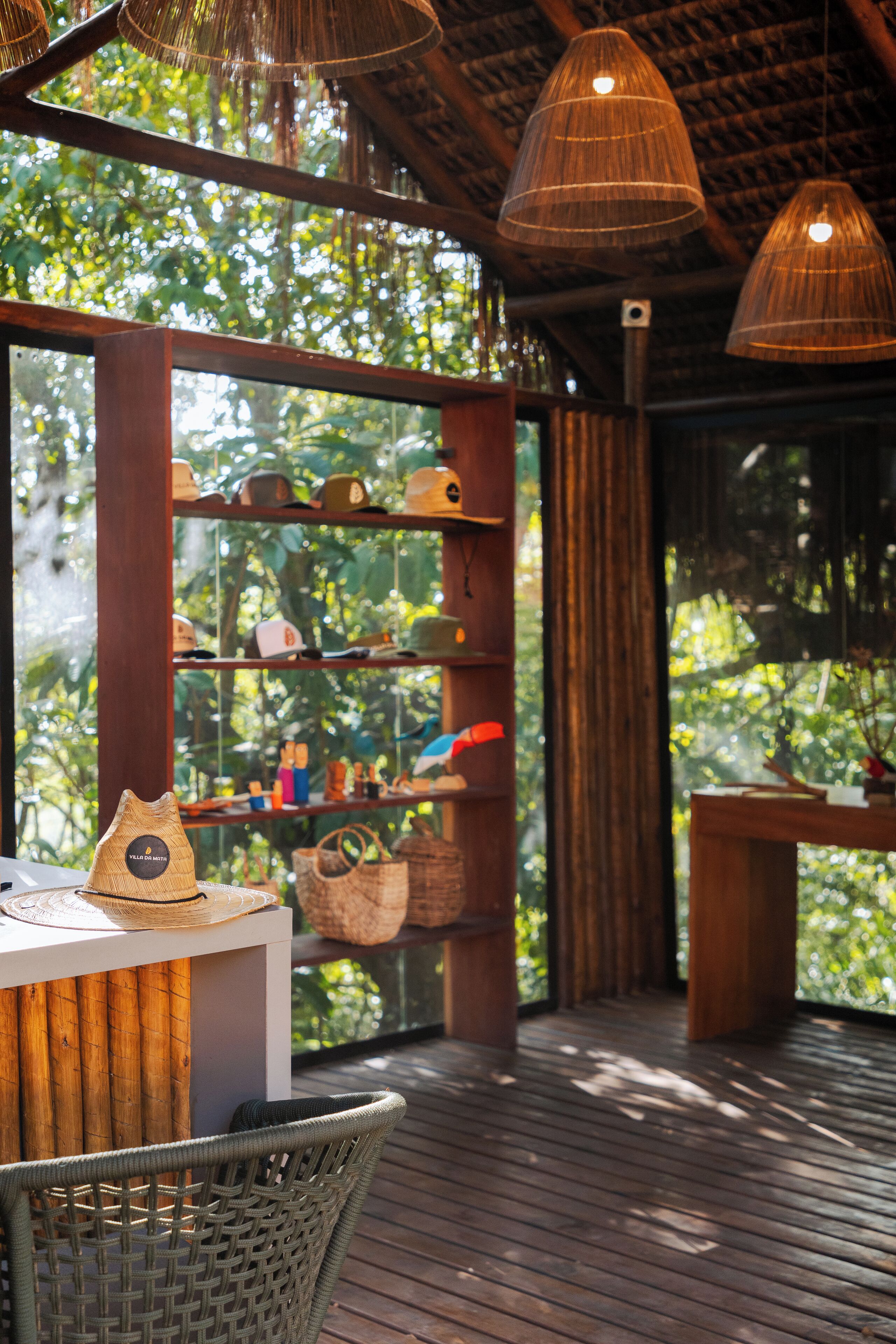 Una terraza de madera con muebles de mimbre, una vitrina con sombreros y vistas a zonas verdes.