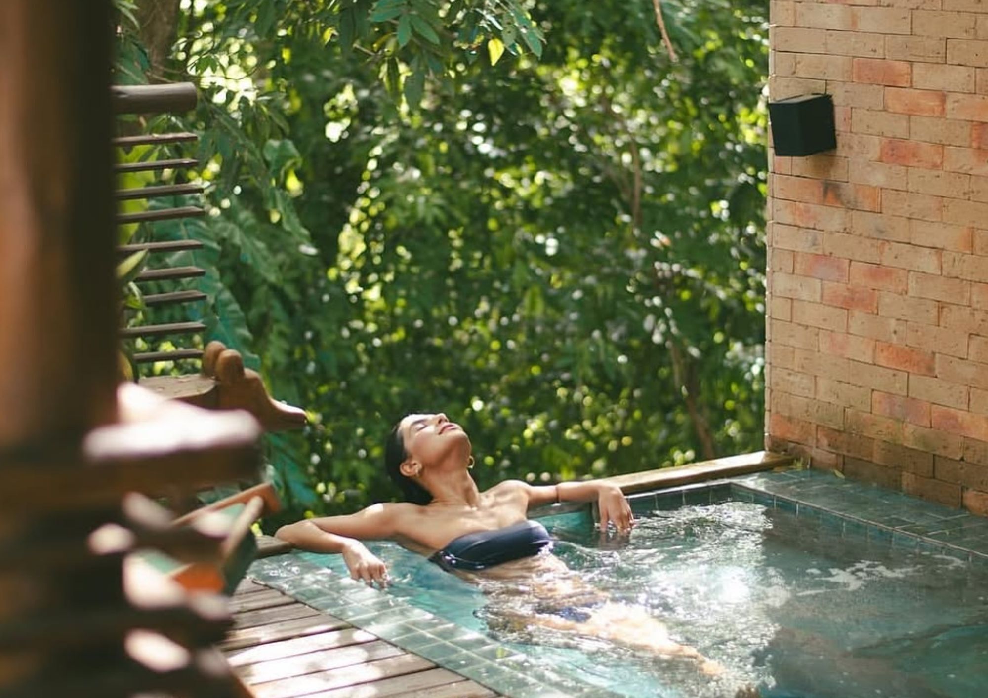 Una persona relajándose en un jacuzzi rodeado de abundante vegetación.