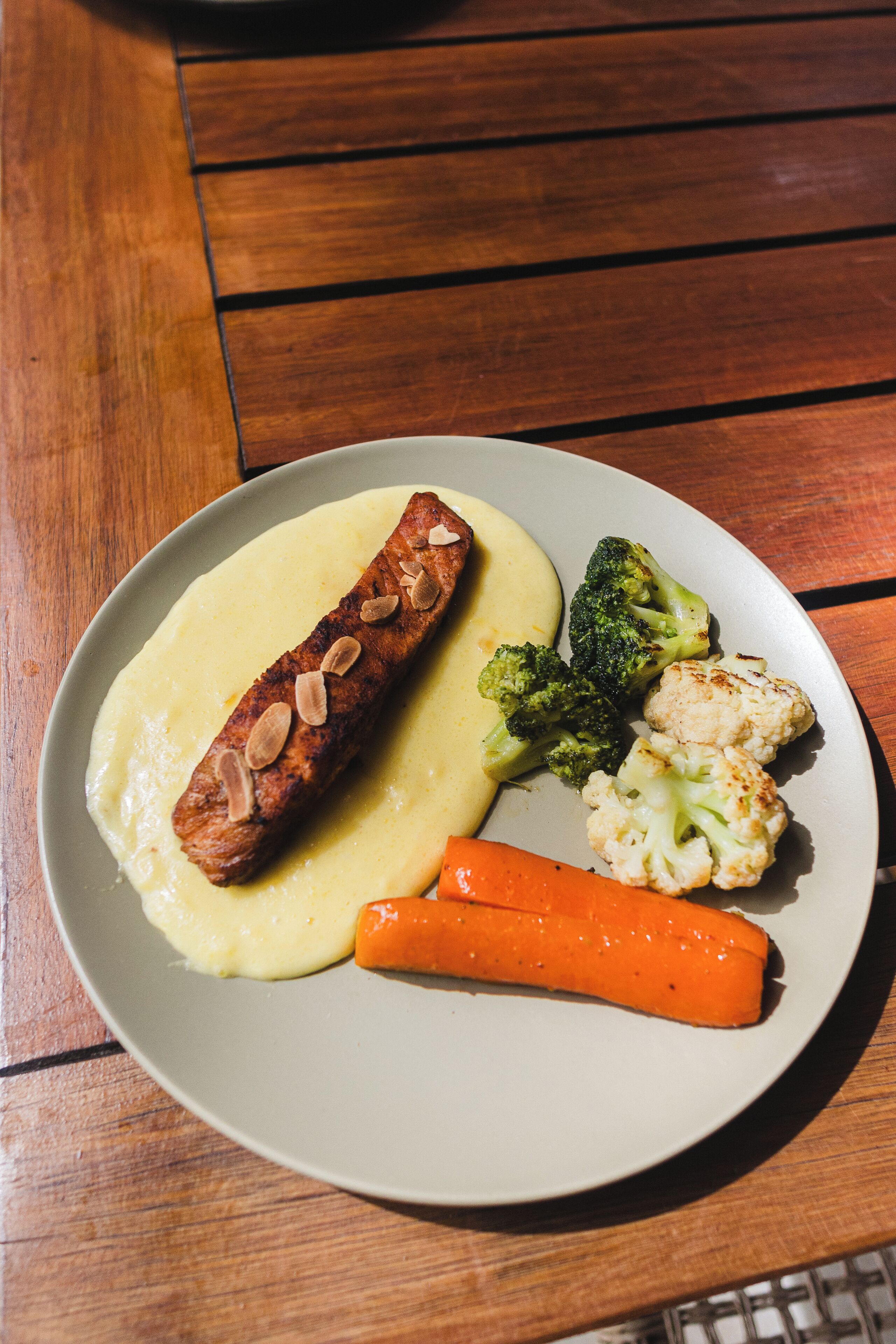 Un plato de comida con salchicha, puré de papas, brócoli, coliflor y zanahoria.