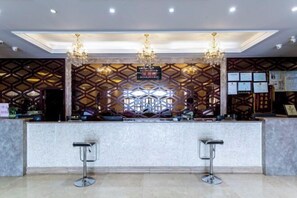 Un área de recepción con diseño moderno, que presenta una pared con patrón geométrico, dos taburetes de bar y una araña.
