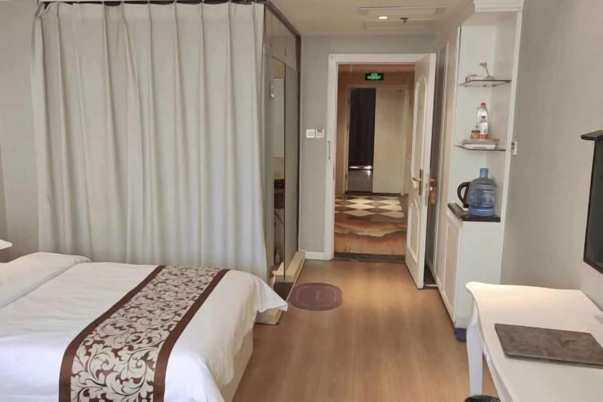 A hotel room with a bed, a bedside table, a water dispenser, and a view of the hallway.