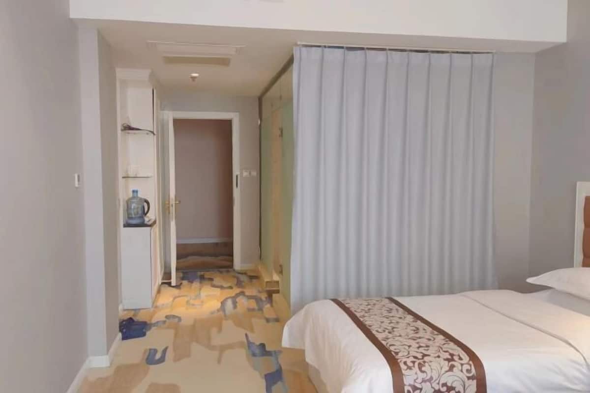 A hotel room with a bed, a bathroom, and a hallway leading to another room.
