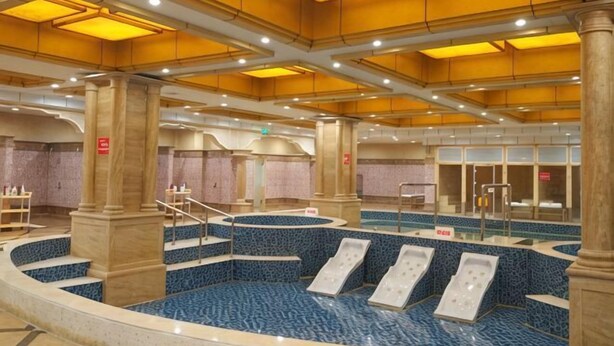 Une vaste piscine intérieure dotée de plusieurs couloirs, entourée de colonnes et recouverte d’un sol carrelé.