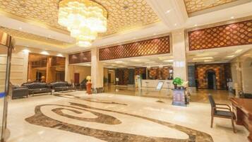 A spacious lobby with a large, ornate chandelier, seating areas, and a decorative floor design.