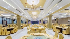 Une salle de banquet avec des tables rondes, des chaises, des lustres et une scène.