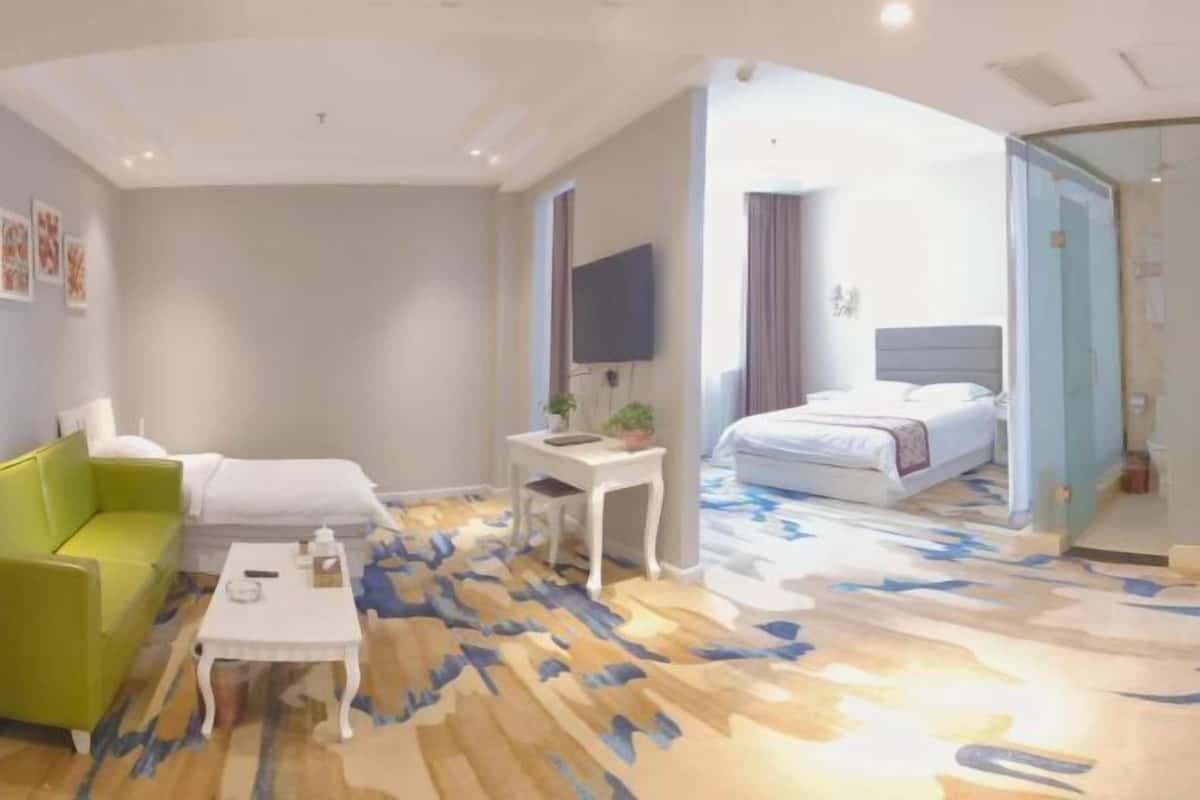 A hotel room with a green sofa, a small white table, a bed with a blue and white patterned bedspread, and a large mirror.