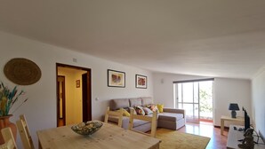 A living room with a wooden dining table, a sofa, and a large window.