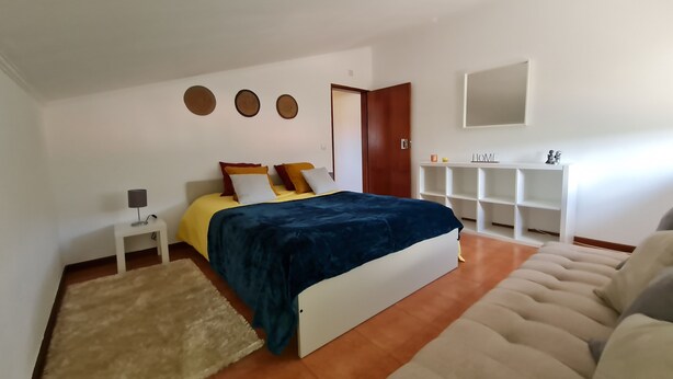 A bedroom with a bed, bedside tables, a wardrobe, a mirror, and a shelf with decorative items.