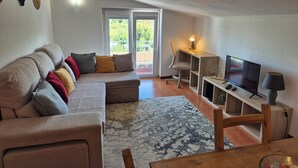 A modern living room with a sectional sofa, a TV, a desk with a lamp, and a balcony door.