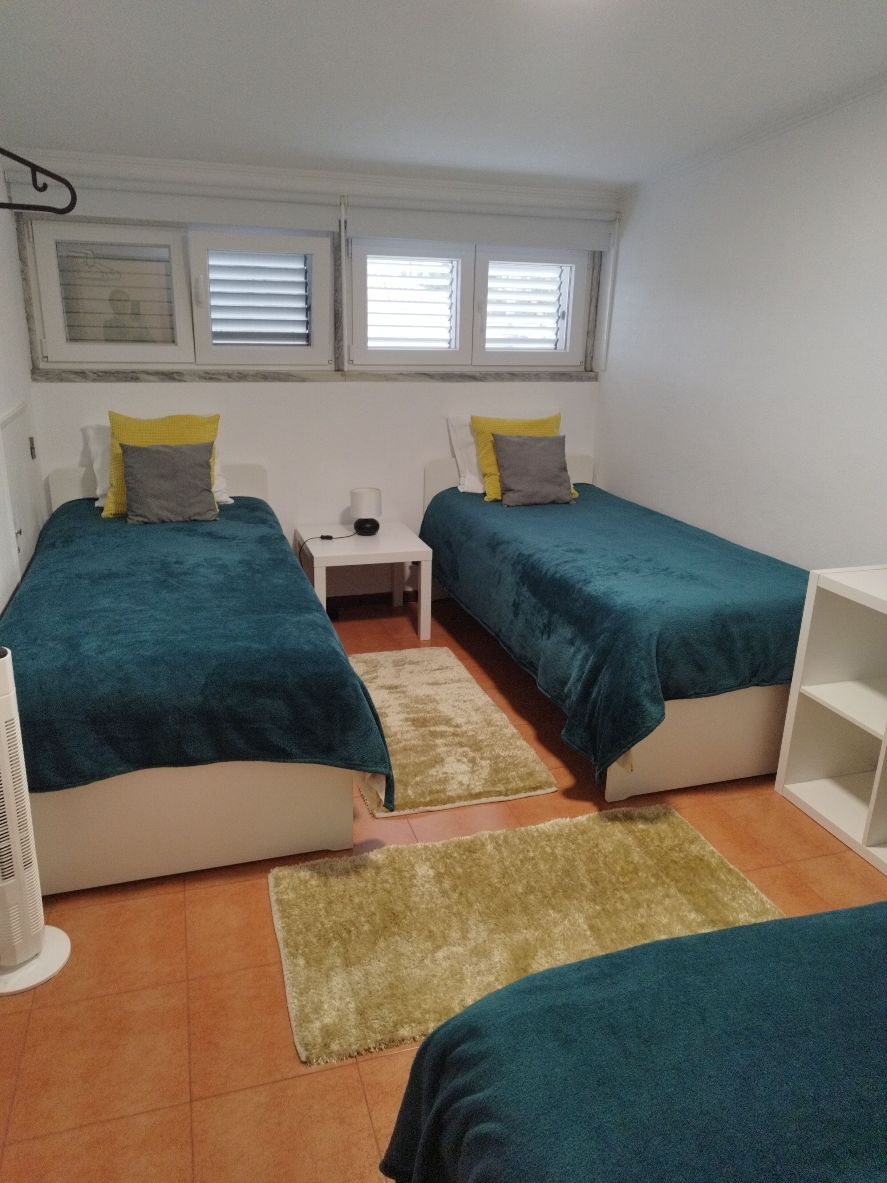 Une chambre avec deux lits, une table de chevet, un radiateur et une fenêtre avec des stores.