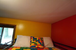 A bed with a colorful quilt, white pillows, and a window with a view of trees.
