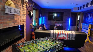 A room with a brick wall, a welcome sign, a television, a sofa, and a foosball table. - Poconos Top Rated Resort - Saw Creek Estates (Bushkill)