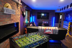 A room with a brick wall, a welcome sign, a television, a sofa, and a foosball table. - Poconos Top Rated Resort - Saw Creek Estates (Bushkill)