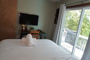 A hotel room with a bed, a desk with a flat-screen TV, a chair, and a view of the outdoors through a balcony. - Poconos Top Rated Resort - Saw Creek Estates (Bushkill)