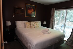 A bedroom with a bed, two bedside lamps, a window with curtains, and a framed picture on the wall.