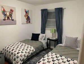 Un dormitorio con dos camas, cada una con una colcha estampada, una mesita de noche pequeña con una lámpara y una ventana con cortinas.