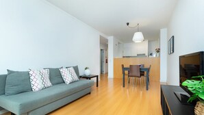 Een moderne woonkamer met een grijze bank, een houten eettafel en een televisie.