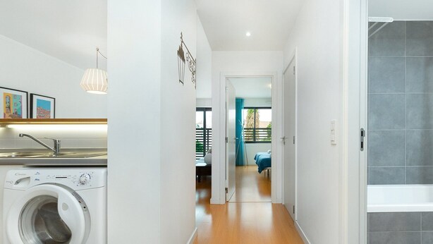 Een modern appartement met een wasruimte, een gang naar een slaapkamer en een badkamer met douche.