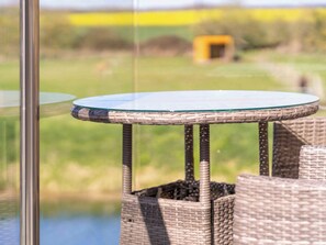 A round glass table with woven wicker legs, positioned near a window overlooking a grassy area.