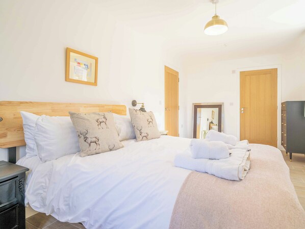 A neatly made bed with white linens and decorative pillows, a bedside table, a wall-mounted lamp, and a wooden door.