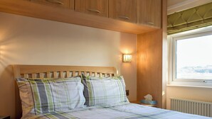 Een net opgemaakt bed met een geruit sprei, een houten hoofdbord en een nachtkastje met een lamp.