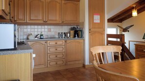 Een keuken met houten kastjes, een aanrecht en een eethoek met een houten tafel en stoelen.