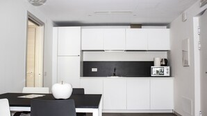 Una cocina moderna con armarios blancos, encimera negra y un microondas. Hay una mesa de comedor con sillas y una manzana blanca encima.