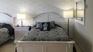 A bedroom with a bed, two bedside tables, a nightstand, a lamp, a mirror, and a patterned wall. - Oceanfront renovated condo on the beach - amazing ocean view (Sunny Isles Beach)