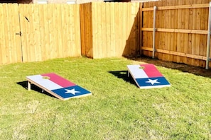 Zwei Rasenspiele mit Texas-Bundesstaat-Flaggen auf einer Rasenfläche, im Hintergrund sind Holzzäune zu sehen.